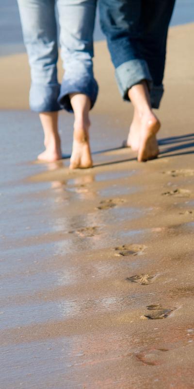 The feet of two people walking side-by-side in beach sand
